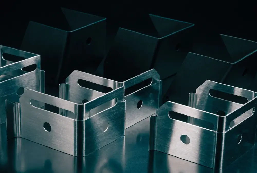 Stack of laser-cut satin aluminium trays and panels on a dark workbench